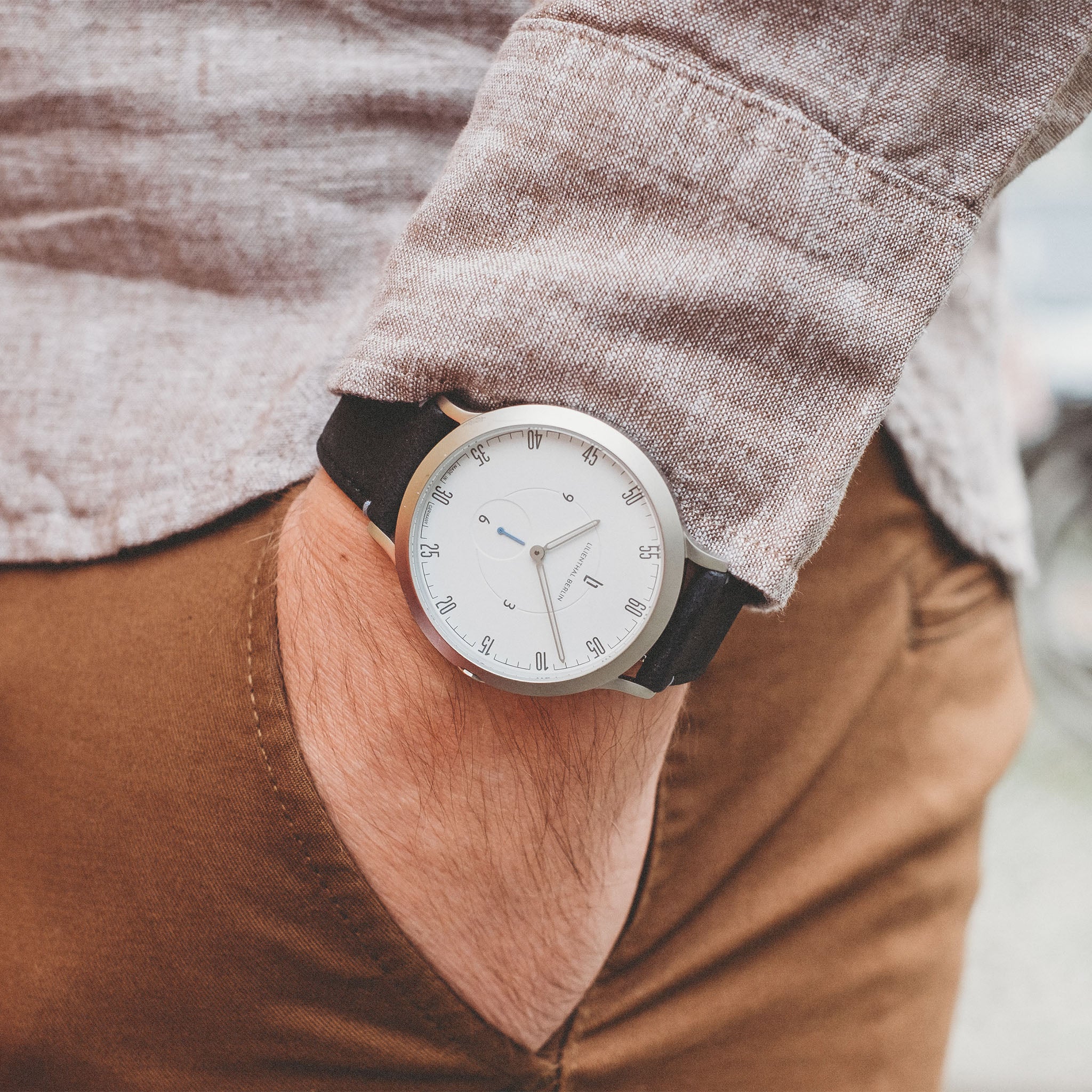Minimalist silver wristwatch with white dial and black strap on a wrist, casual outfit style