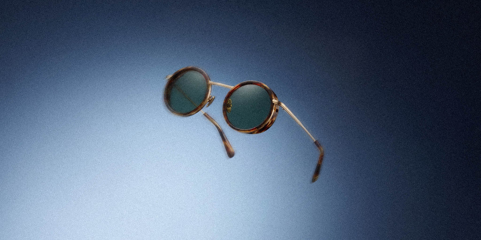 Round tortoiseshell sunglasses with dark lenses on a gradient blue background