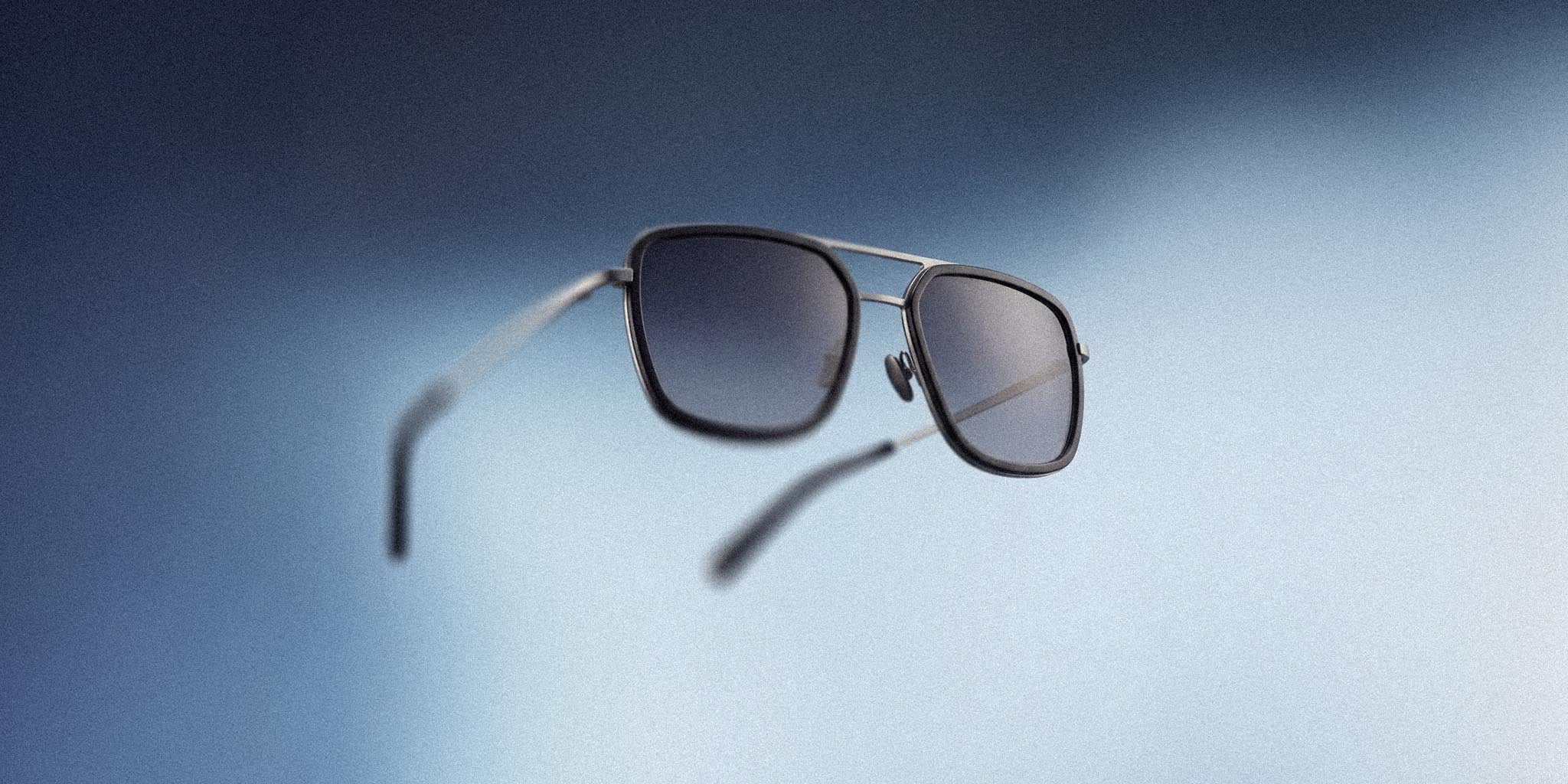 Modern square aviator sunglasses with black frames and tinted lenses on a blue gradient background