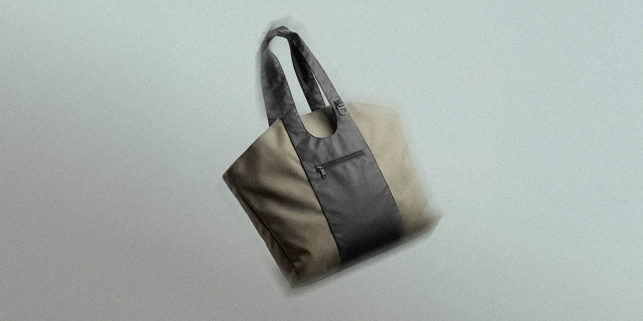 Modern two-tone tote bag with black handles and front zipper pocket on neutral background
