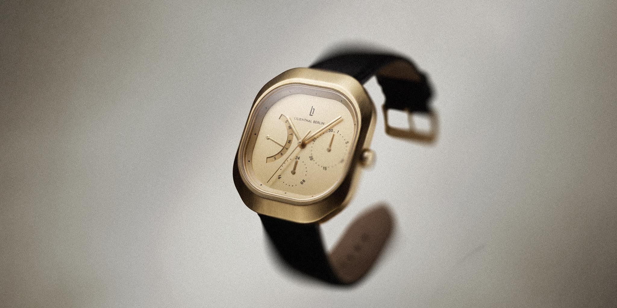 Modern silver and gold square watch with cream dial and black strap on light background