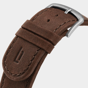 Close-up of brown leather watch strap with silver buckle and embossed detail