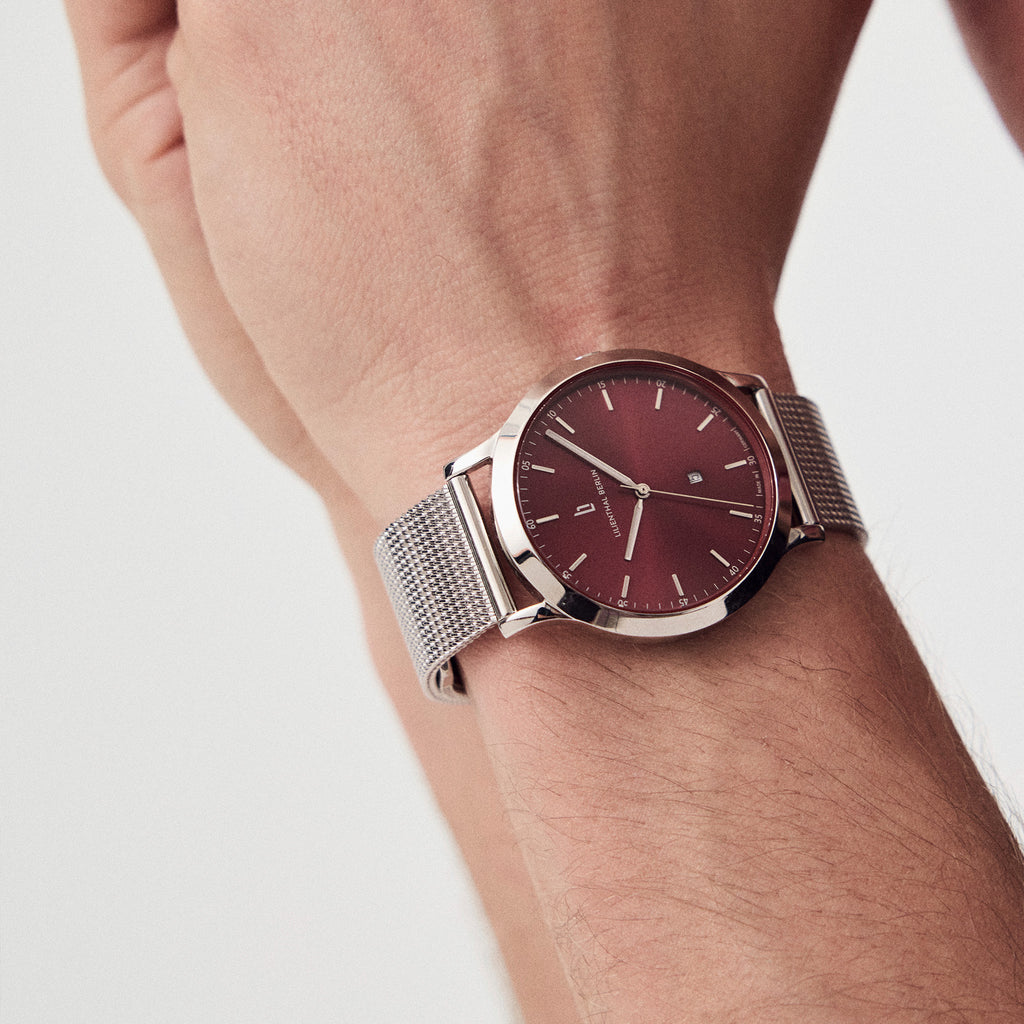 Silver mesh strap watch with burgundy dial and minimalist design on wrist