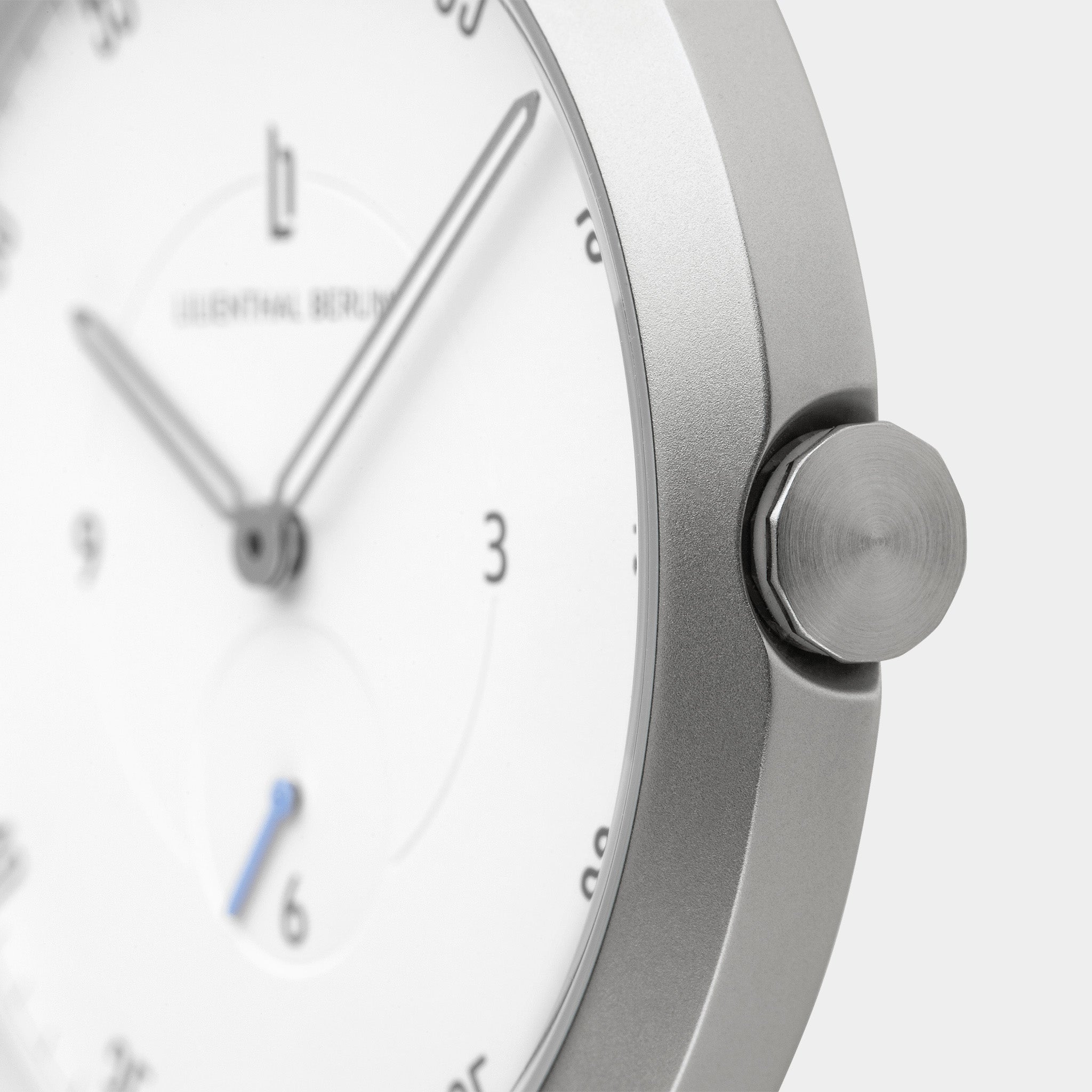 Minimalist silver wristwatch with white dial, sleek hands, and brushed metal crown close-up